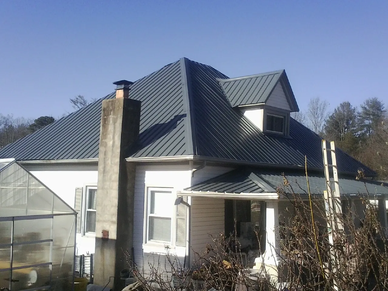 Dark blue standing seam metal roof on a white farmhouse with dormer — Slate & Tile Roof Repair by Roofing Brothers in Langsville
