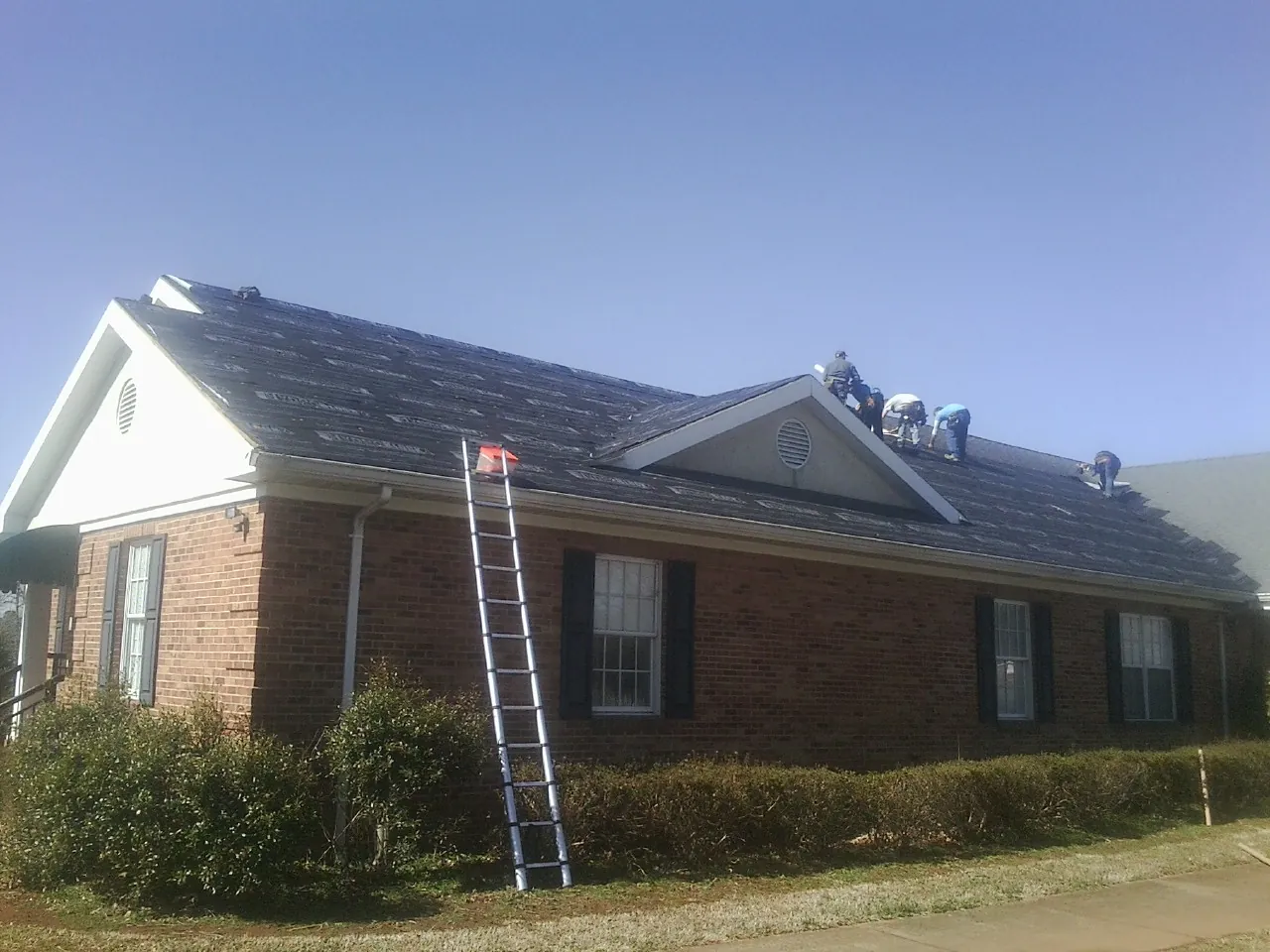 Crew tearing shingles off a brick ranch roof with a ladder set — Metal Roof Repair work by our crew in Langsville