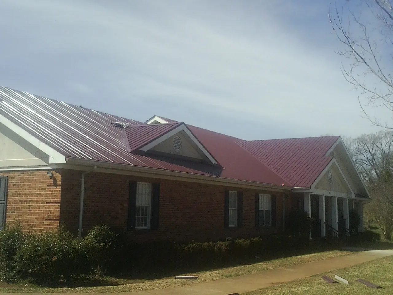 Red metal roof with gabled entries on a long brick building, from a Hail Damage Roof Repair job in Langsville