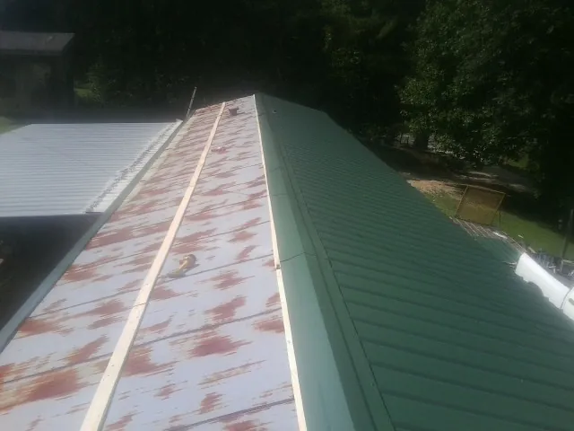 Old rusted panels beside newly installed green metal roofing — Wind Damage Roof Repair by Roofing Brothers in Langsville