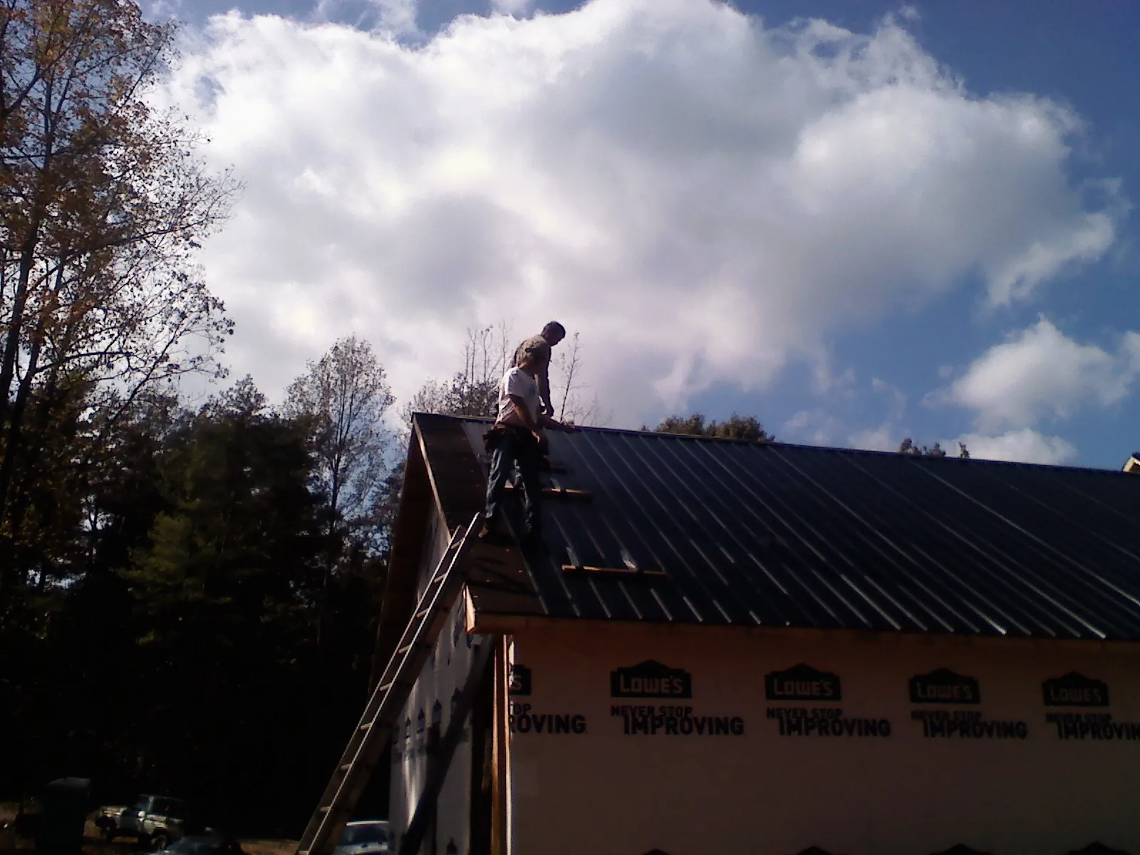Roofer fastening dark metal panels high against a cloudy sky, from a Roof Inspection job in Langsville