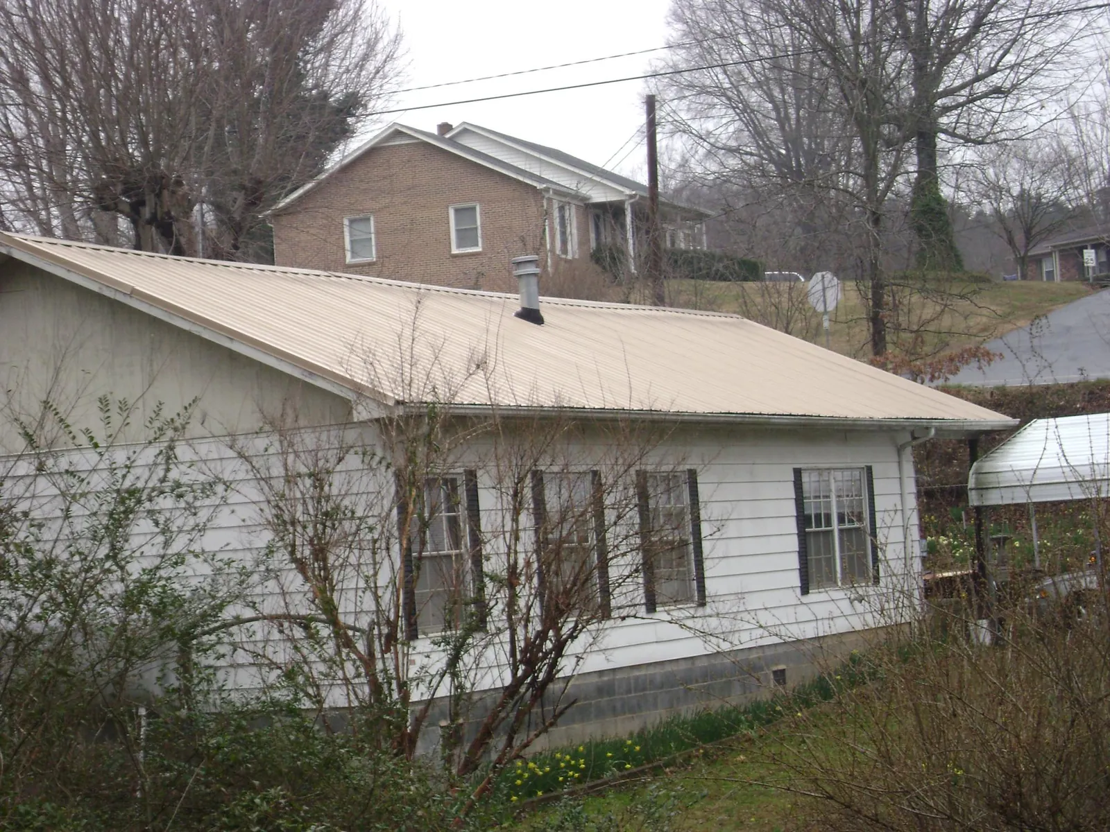 Tan metal roof on a white sided house set into a hillside — Commercial Roofing by Roofing Brothers in Langsville